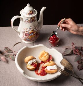 Teekanne mit altem Muster, davor weißer Teller mit Scones mit Frischkäse und Erdbeermarmelade